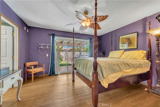 bedroom with ceiling fan, a textured ceiling, access to exterior, baseboards, and wood finished floors
