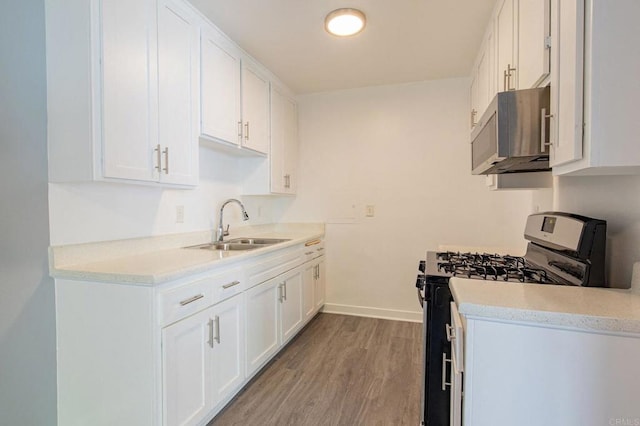 kitchen with light wood-type flooring, stainless steel microwave, white cabinets, range with gas cooktop, and a sink