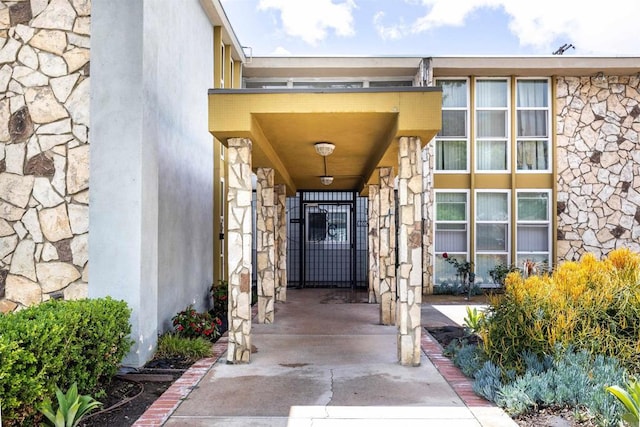 view of exterior entry featuring a gate, stone siding, and stucco siding