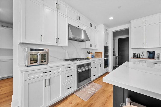 kitchen with recessed lighting, under cabinet range hood, white cabinets, light wood-style flooring, and stainless steel appliances