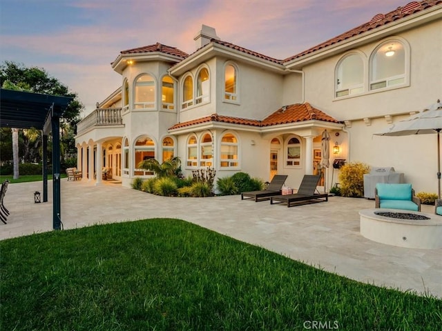 back of property at dusk with stucco siding, a fire pit, a patio area, and a balcony