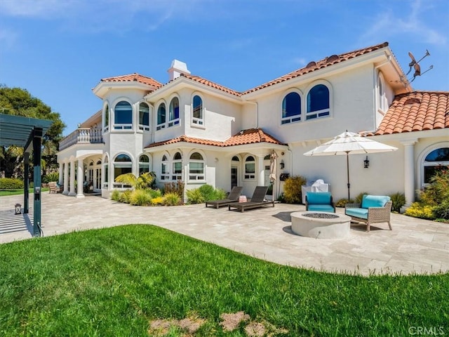 rear view of property featuring a patio, a chimney, a balcony, and an outdoor fire pit