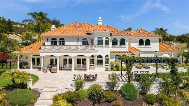 back of property with french doors, a balcony, a patio area, and a chimney