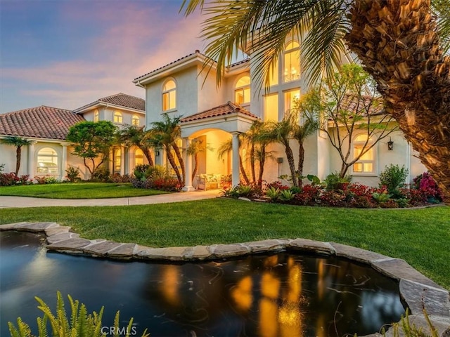 mediterranean / spanish-style house with a lawn, stucco siding, and a tile roof