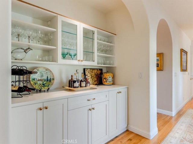 bar featuring light wood-style floors, arched walkways, and baseboards