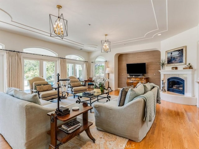 living room featuring light wood finished floors, arched walkways, a chandelier, a glass covered fireplace, and recessed lighting