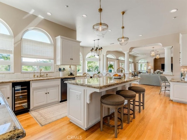 kitchen featuring decorative columns, dishwasher, a sink, wine cooler, and white cabinetry