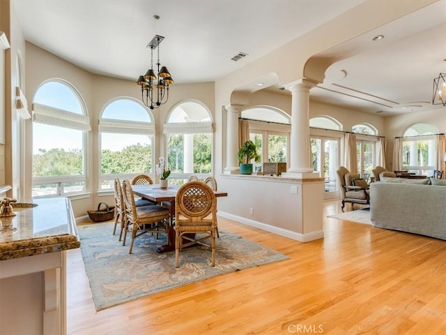 dining room with light wood-type flooring, ornate columns, a chandelier, and visible vents