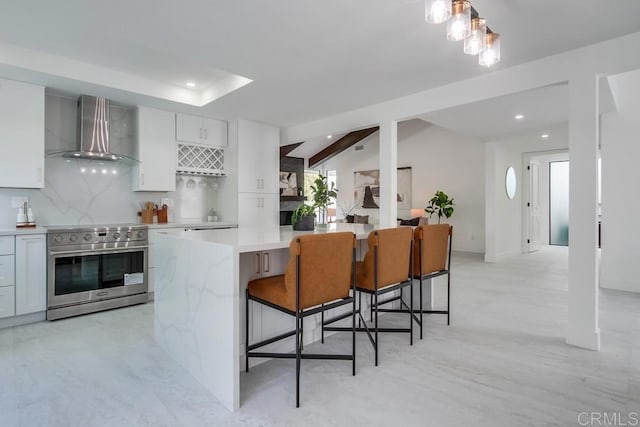 kitchen with recessed lighting, light countertops, wall chimney exhaust hood, white cabinetry, and high end range