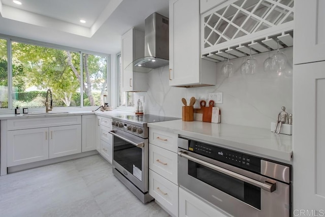 kitchen featuring light countertops, wall chimney exhaust hood, white cabinetry, a sink, and stainless steel appliances
