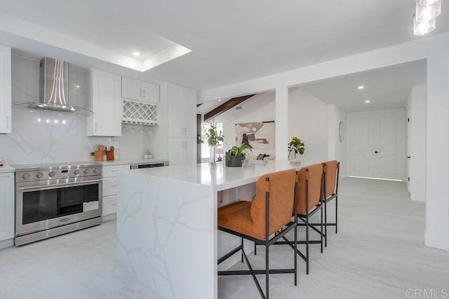 kitchen with a breakfast bar area, wall chimney exhaust hood, stainless steel stove, recessed lighting, and white cabinetry