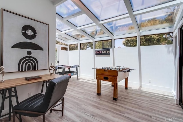 game room featuring a skylight, baseboards, light wood finished floors, and beam ceiling