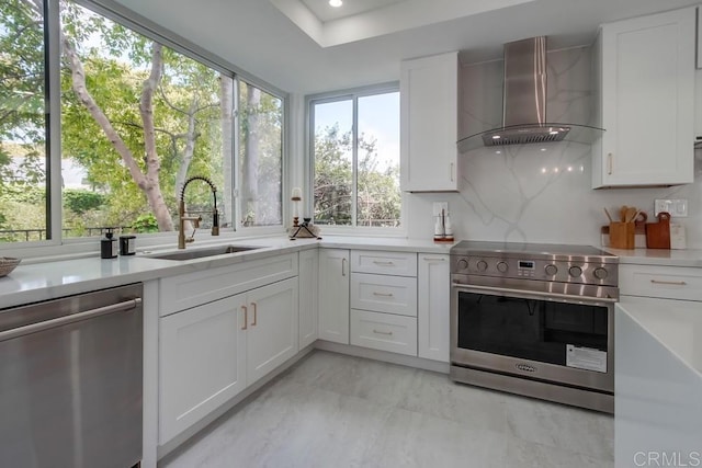kitchen featuring a sink, light countertops, white cabinets, stainless steel appliances, and wall chimney exhaust hood