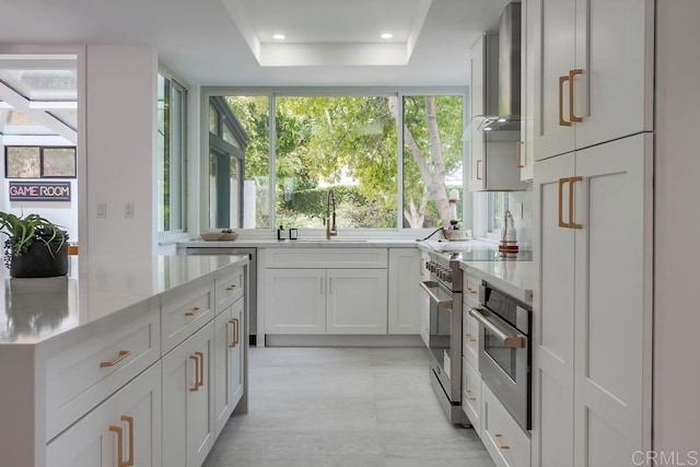 kitchen featuring recessed lighting, wall chimney exhaust hood, white cabinets, a sink, and appliances with stainless steel finishes