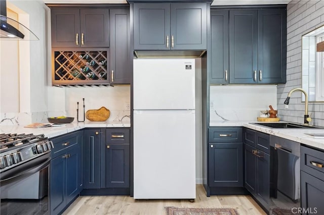 kitchen featuring wall chimney range hood, light stone counters, a sink, backsplash, and stainless steel appliances