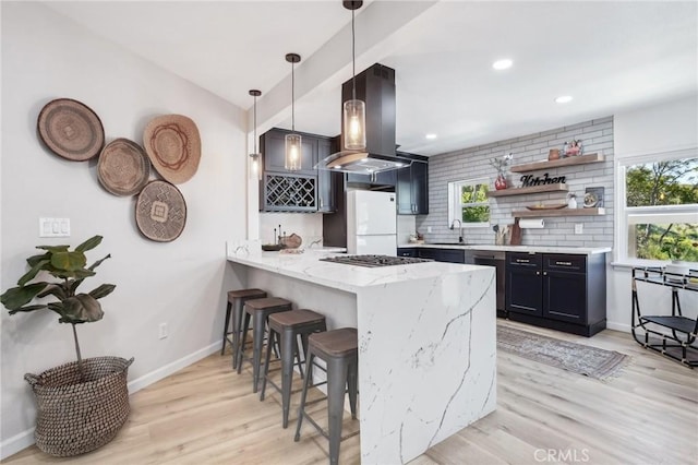 kitchen featuring a breakfast bar area, light wood-style flooring, stainless steel appliances, a peninsula, and island range hood