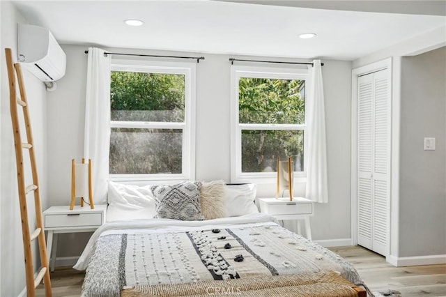 bedroom with recessed lighting, baseboards, a wall mounted AC, and light wood-type flooring