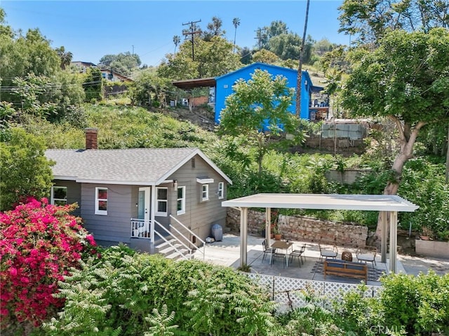 back of house with a patio, a shingled roof, and a chimney