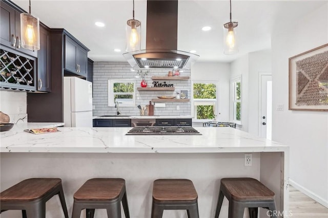kitchen featuring freestanding refrigerator, stainless steel gas cooktop, a peninsula, tasteful backsplash, and island exhaust hood