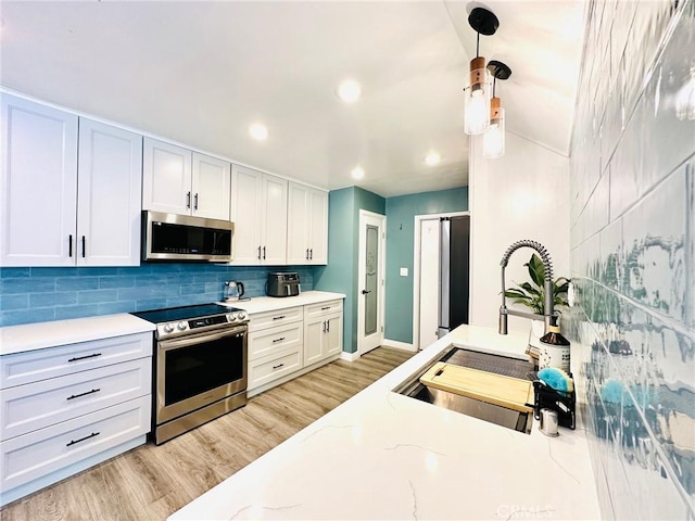 kitchen with white cabinets, a sink, light wood-style floors, stainless steel appliances, and backsplash
