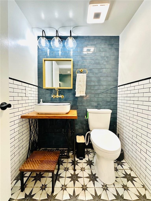 bathroom with toilet, tile walls, a sink, and a wainscoted wall