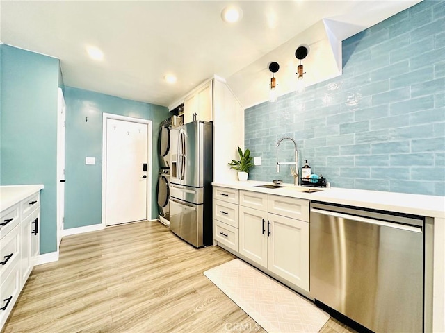 kitchen featuring stacked washer and clothes dryer, light countertops, a sink, appliances with stainless steel finishes, and backsplash