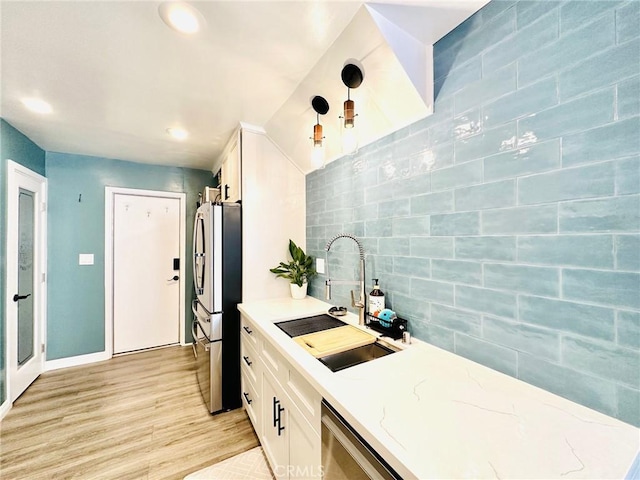 kitchen featuring decorative backsplash, appliances with stainless steel finishes, light wood-type flooring, a sink, and white cabinets