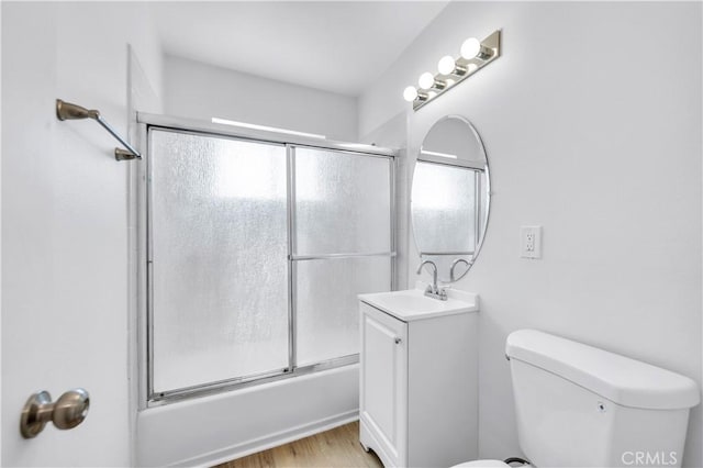 bathroom featuring toilet, wood finished floors, bath / shower combo with glass door, and vanity