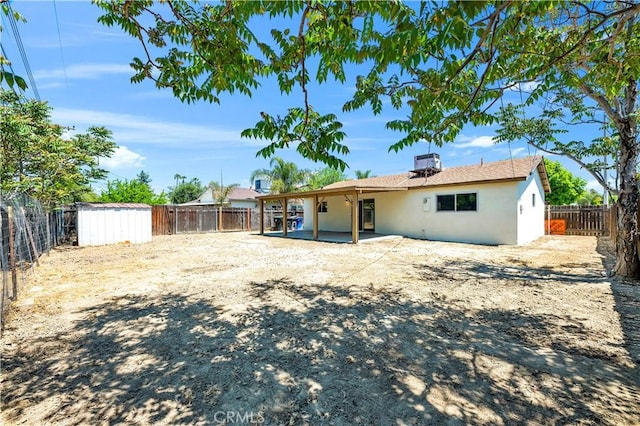 rear view of property with an outdoor structure, a fenced backyard, stucco siding, a storage unit, and a patio area