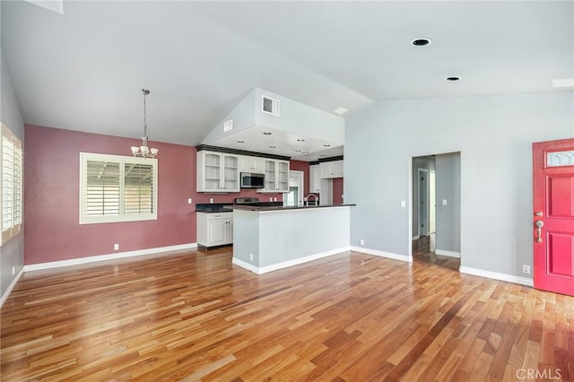 kitchen featuring an inviting chandelier, lofted ceiling, dark countertops, light wood-type flooring, and stainless steel microwave