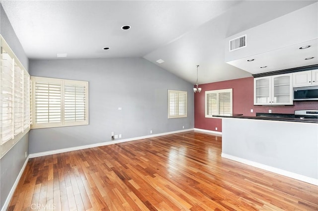 kitchen with dark countertops, appliances with stainless steel finishes, light wood-style floors, lofted ceiling, and visible vents