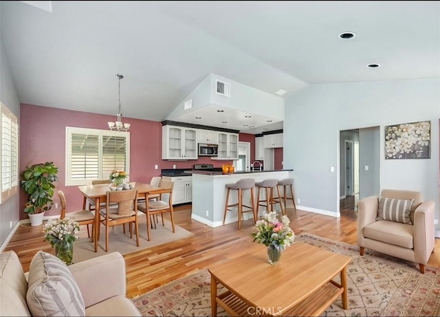 living area with a chandelier, visible vents, baseboards, light wood finished floors, and lofted ceiling