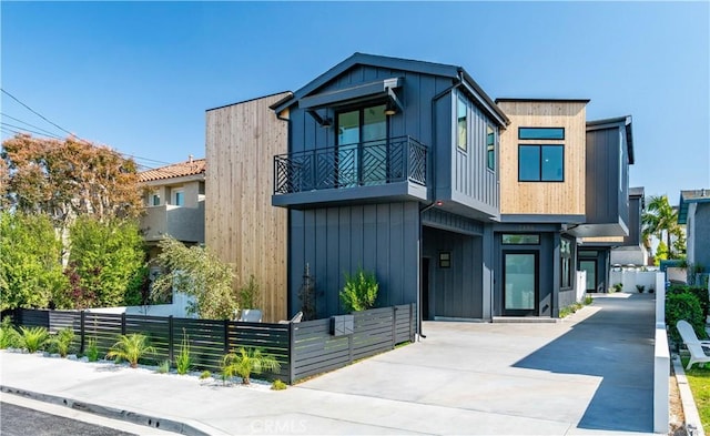 contemporary home featuring concrete driveway, board and batten siding, a fenced front yard, and a balcony