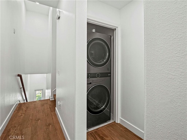 washroom with baseboards, laundry area, stacked washing maching and dryer, and wood finished floors