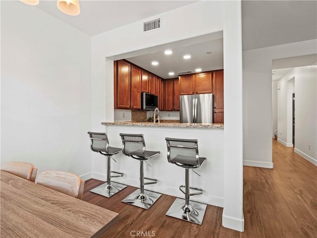 kitchen with visible vents, wood finished floors, a kitchen breakfast bar, recessed lighting, and stainless steel appliances