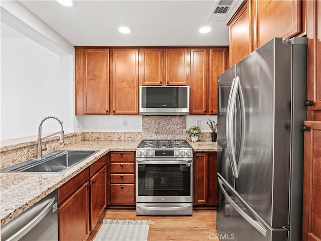 kitchen with a sink, light stone counters, stainless steel appliances, and light wood finished floors
