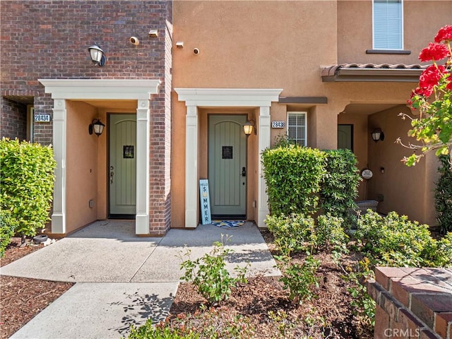 view of exterior entry with stucco siding and brick siding