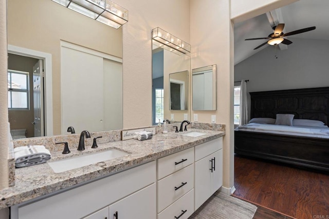 full bath with a sink, double vanity, vaulted ceiling, and wood finished floors