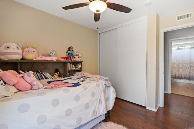 bedroom with a closet, visible vents, wood finished floors, baseboards, and a ceiling fan