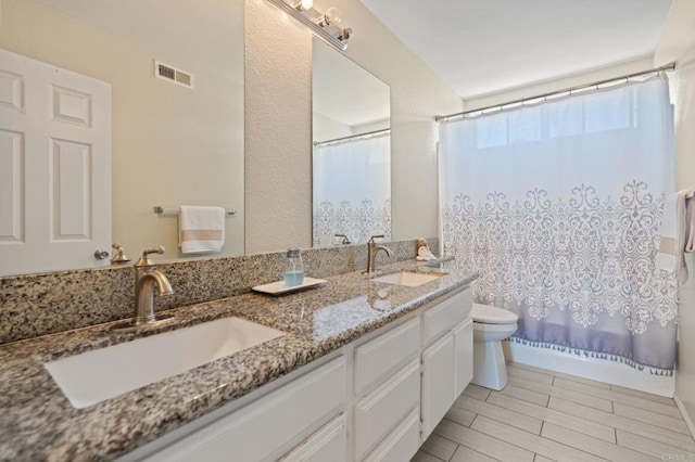 full bathroom with visible vents, a sink, double vanity, and toilet