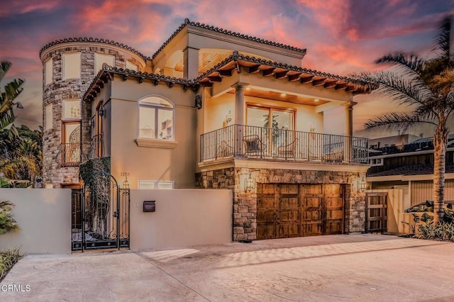 mediterranean / spanish-style home with fence, a balcony, stone siding, a gate, and concrete driveway