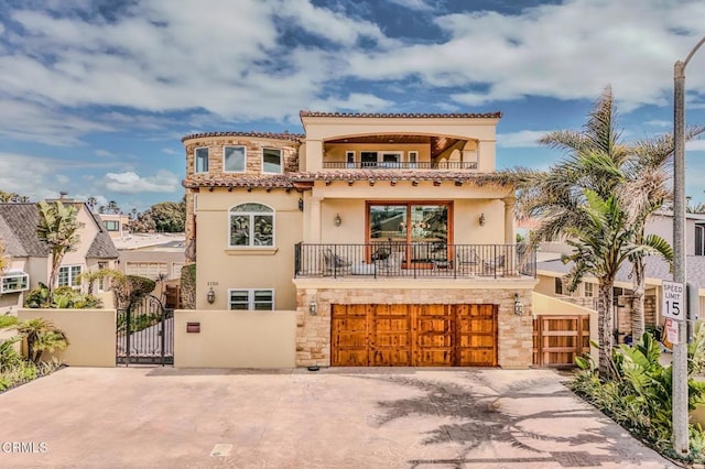 mediterranean / spanish-style home with a garage, a gate, a balcony, and stone siding