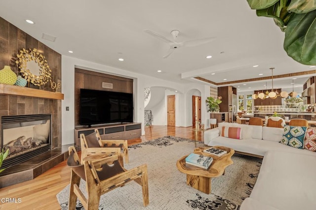 living room featuring a ceiling fan, a tiled fireplace, arched walkways, wood finished floors, and recessed lighting
