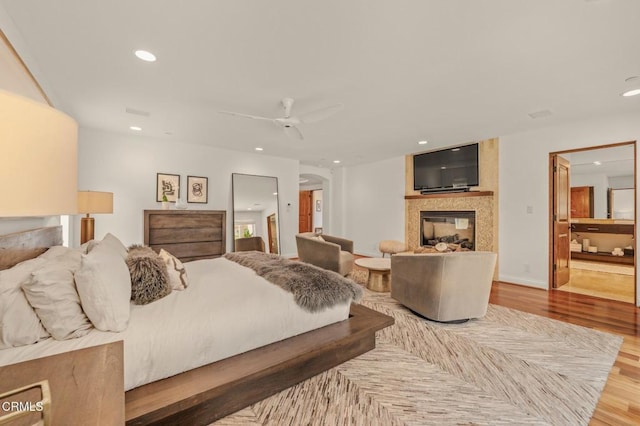 bedroom with a multi sided fireplace, ceiling fan, arched walkways, wood finished floors, and recessed lighting
