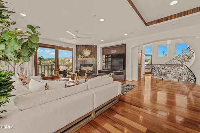 living area featuring a ceiling fan, arched walkways, a large fireplace, recessed lighting, and light wood-style flooring