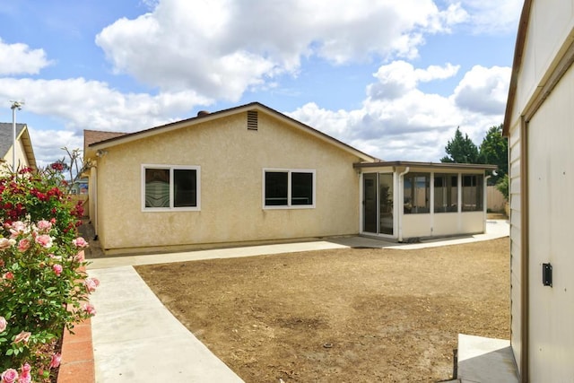 rear view of property featuring stucco siding, a sunroom, and a patio area