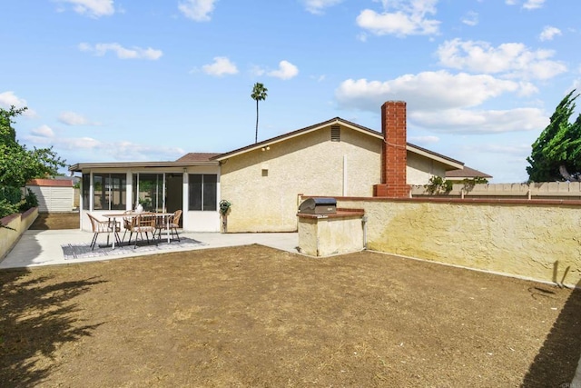 back of property with a chimney, a sunroom, a patio area, fence, and stucco siding