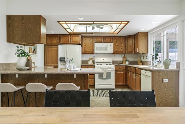 kitchen featuring brown cabinets, a sink, white appliances, a peninsula, and recessed lighting
