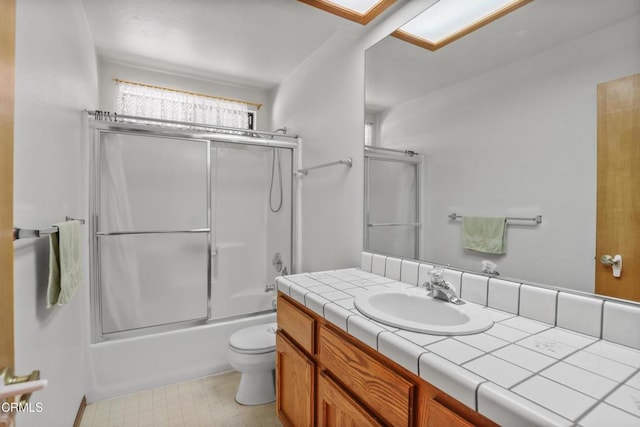 bathroom with a skylight, vanity, enclosed tub / shower combo, and toilet