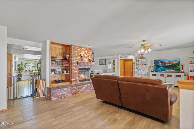 living room with ceiling fan, a brick fireplace, and light wood-style flooring